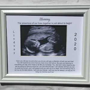 May include: A white picture frame with a black and white ultrasound image inside. The frame has the text "Mommy. The adventure of our lives together is just about to begin!" and "Lindsay 2020" printed on it.