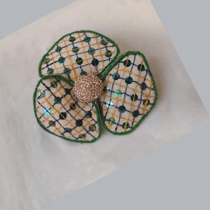 Può includere: Spilla a forma di fiore in tessuto con tre petali. I petali sono bianchi con un motivo a griglia gialla e nera, bordi verdi e paillettes turchesi. Il centro è una sfera strutturata color beige.