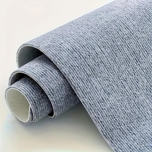 May include: A rolled-up section of gray textured fabric with a white backing. The fabric has a woven appearance, with visible horizontal lines. The edges of the roll reveal the white underside, creating a contrast with the gray exterior.