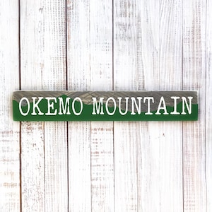 May include: A wooden sign with a green background and white text that reads "OKEMO MOUNTAIN".