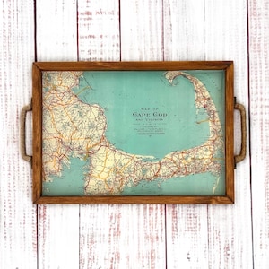 May include: A wooden serving tray with rope handles features a vintage map of Cape Cod and vicinity. The map is printed on a light blue background with orange and yellow roads.