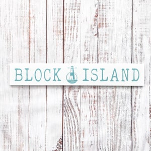 May include: White wooden sign with blue text that reads "BLOCK ISLAND" with a blue lighthouse icon in the middle.