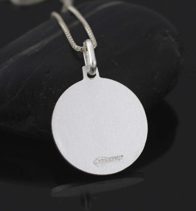 May include: A silver oval pendant with a smooth, polished surface. The pendant is attached to a silver chain.