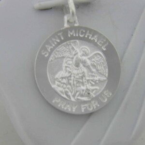 May include: Silver pendant featuring a depiction of Saint Michael the Archangel with the words "Saint Michael Pray For Us" around the edge.