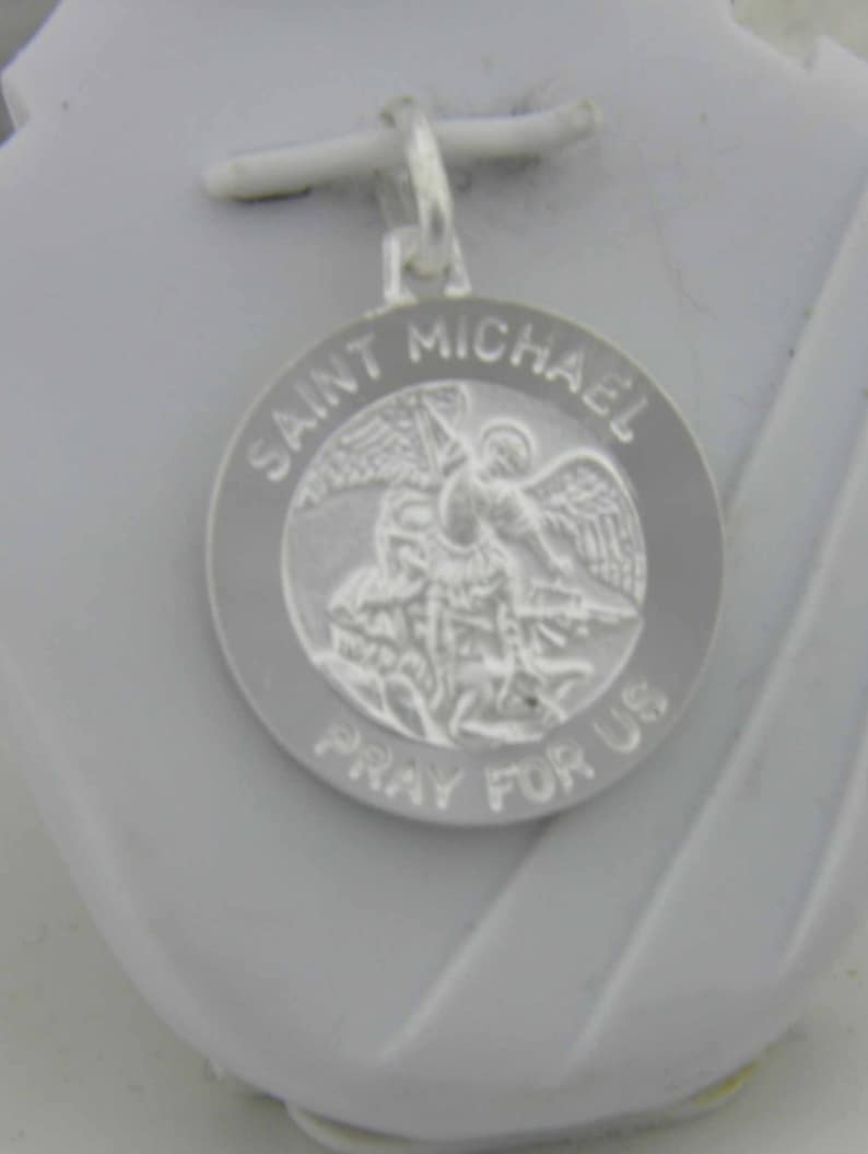 May include: Silver pendant featuring a depiction of Saint Michael the Archangel with the words "Saint Michael Pray For Us" around the edge.