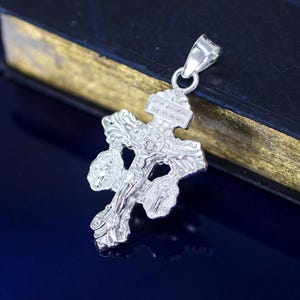 May include: Silver pendant featuring a detailed ornate cross with a figure of Jesus Christ. The cross has a decorative design with intricate details.