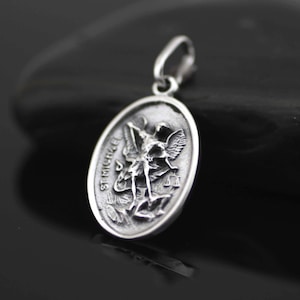 May include: Silver pendant featuring a detailed depiction of Saint Michael the Archangel, with the inscription "St. Michael" on the side.