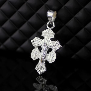 Puede incluir: Pendiente de plata con un crucifijo detallado y tres medallones. El crucifijo representa a Jesucristo en la cruz, y los medallones presentan imágenes religiosas. El pendiente tiene un bucle en la parte superior para sujetarlo a una cadena.