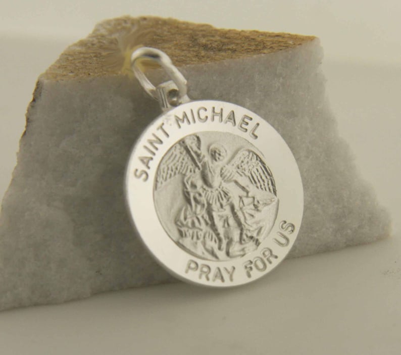 May include: Silver pendant featuring a depiction of Saint Michael the Archangel with the inscription "Saint Michael Pray For Us".