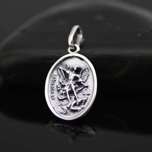 May include: Silver pendant featuring a detailed depiction of Saint Michael the Archangel, with the inscription "ST MICHAEL" on the edge.