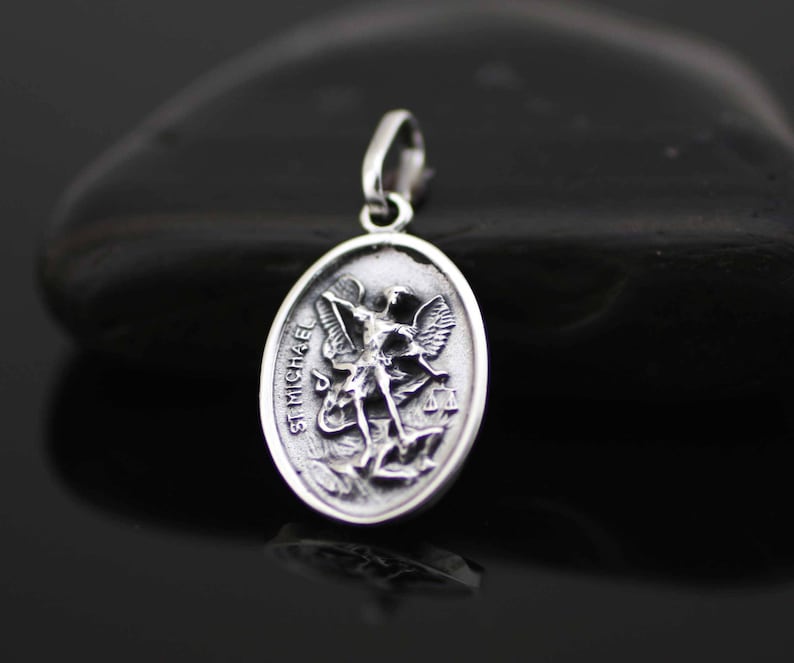 May include: Silver pendant featuring a detailed depiction of Saint Michael the Archangel, with the inscription "ST MICHAEL" on the edge.