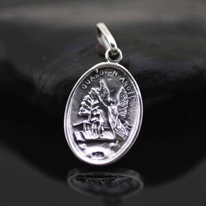 May include: Silver oval pendant with a guardian angel design. The pendant has the words "Guardian Angel" inscribed around the edge.