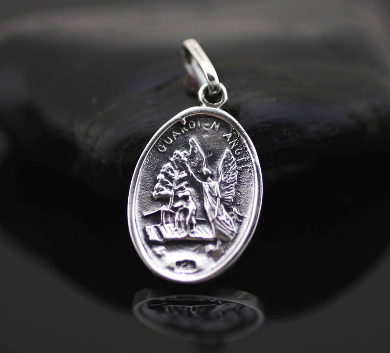 May include: Silver oval pendant with a guardian angel design. The pendant has the words "Guardian Angel" inscribed around the edge.