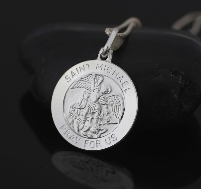 May include: Silver pendant featuring a detailed image of Saint Michael the Archangel slaying a dragon. The pendant is inscribed with "Saint Michael Pray For Us".