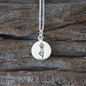 May include: A silver necklace with a round pendant featuring a stylized image of a person in a yoga pose.