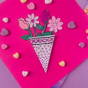 Może przedstawiać: Różowy papierowy stożek wypełniony papierowymi kwiatami i otoczony serduszkami z napisami takimi jak "Kiss Me" i "Be Mine".