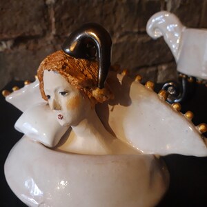 May include: A white ceramic sculpture of a woman with a gold crown and a gold horn on her head. The sculpture is resting on a white pillow.