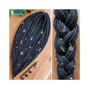 May include: Black synthetic dreadlocks with silver charms, including stars, moons, and pentacles. The dreadlocks are braided together in a three-strand braid.