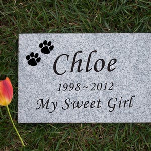May include: A gray granite pet memorial stone with two paw prints and the inscription "Chloe 1998-2012 My Sweet Girl".