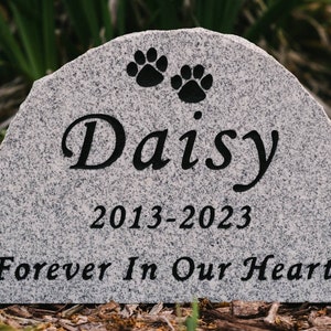 May include: A gray granite pet memorial stone with the inscription "Daisy 2013-2023 Forever In Our Hearts" and two paw prints.