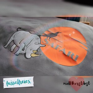 May include: Gray t-shirt with a rhino and a black bird on an orange circle with the word "SAFARI" printed on it. The shirt has the text "fusselfreies" and "melHerzArzt" printed on it.