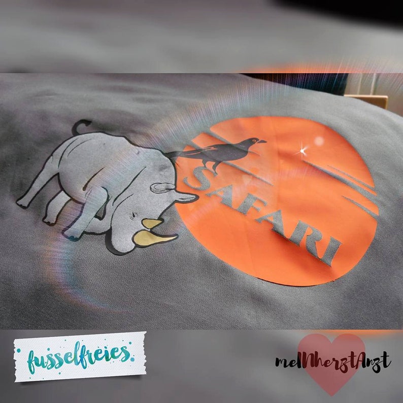 May include: Gray t-shirt with a rhino and a black bird on an orange circle with the word "SAFARI" printed on it. The shirt has the text "fusselfreies" and "melHerzArzt" printed on it.