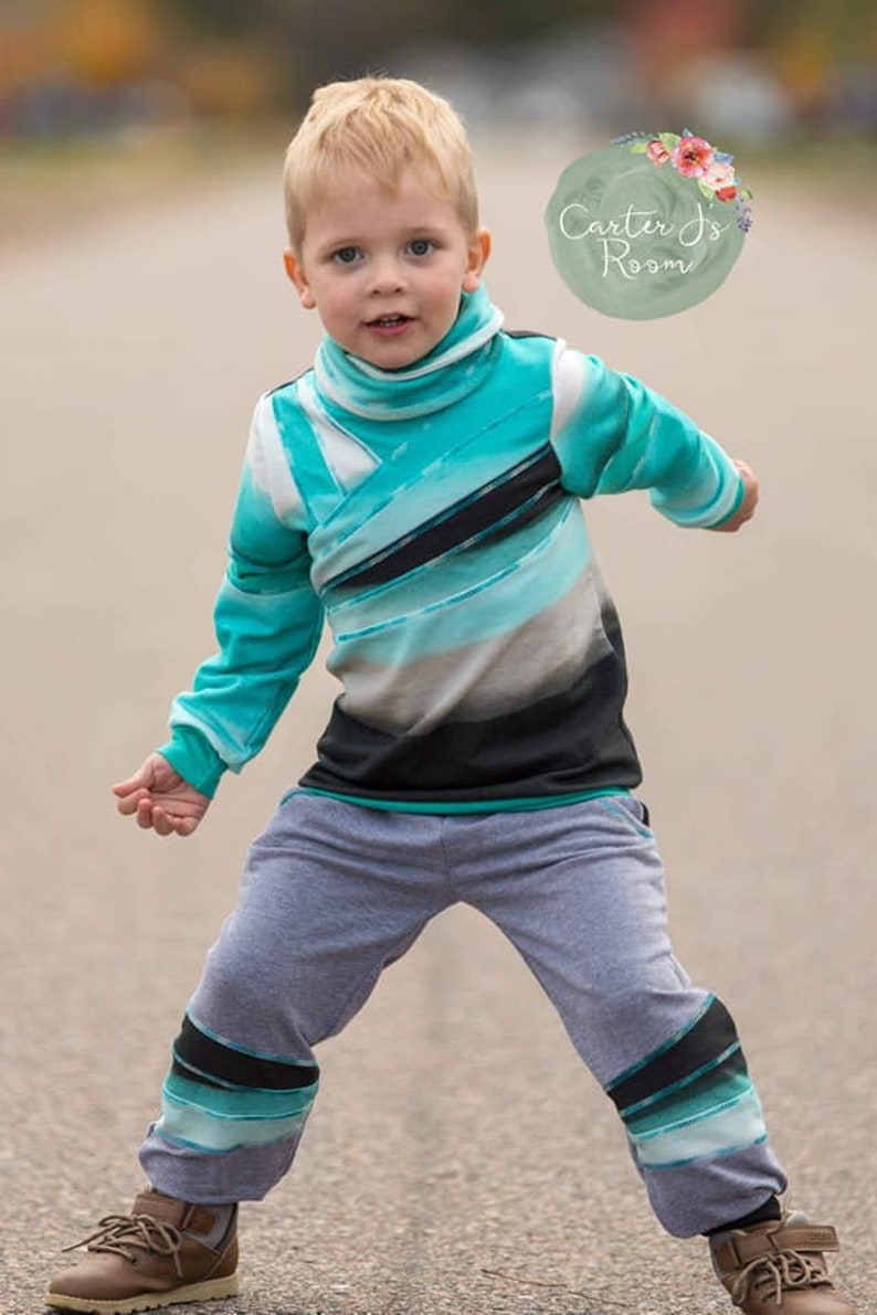May include: A young boy wearing a teal, black, and white striped long-sleeved shirt with a high neck and gray sweatpants with teal, black, and white stripes on the legs. The boy is standing on a paved surface. The image includes the text "Carter's Room".