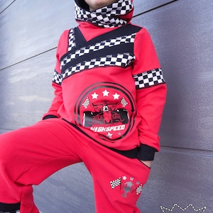 May include: Red hooded sweatshirt and matching sweatpants with black and white checkered accents. The sweatshirt features a black and white graphic of a race car with the text "High Speed". The sweatpants have a black and white graphic of a checkered flag and stars on the left leg.