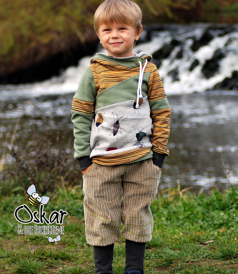May include: A young boy wearing a green, yellow, and white striped hoodie with a bug print. The hoodie has a zipper and a drawstring. The boy is also wearing brown corduroy pants.