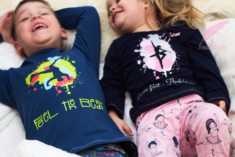 Op de afbeelding: Twee kinderen dragen shirts met lange mouwen met kleurrijke grafische ontwerpen. Het shirt van de jongen zegt "Feel the Beat" en heeft een silhouet van een danser. Het shirt van het meisje heeft een roze en zilveren splatterontwerp met een silhouet van een ballerina en de tekst "Dance first - Think later".