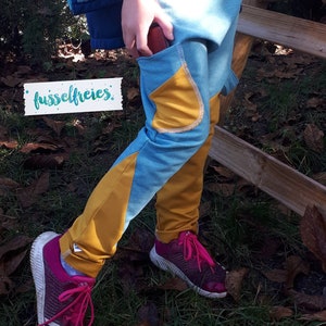 Puede incluir: Un par de leggings azules y amarillas con un bolsillo en el lateral. Las leggings est&aacute;n hechas de una tela suave y c&oacute;moda y tienen un ajuste holgado. El texto "fusselfreies" es visible en una etiqueta blanca.