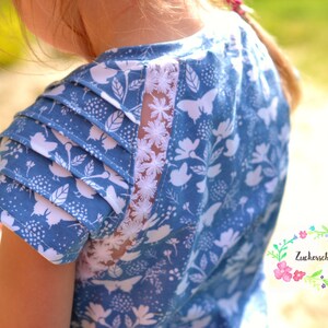 May include: A blue and white patterned dress with a white lace panel on the back. The dress has a ruffled sleeve and a round neckline.