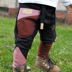 Puede incluir: Pantalones de ch&aacute;ndal negros con detalles en tejido rojo y marr&oacute;n. Los pantalones tienen una cintura con cord&oacute;n y un peque&ntilde;o parche con el texto "lisabelly" en el bolsillo delantero izquierdo.
