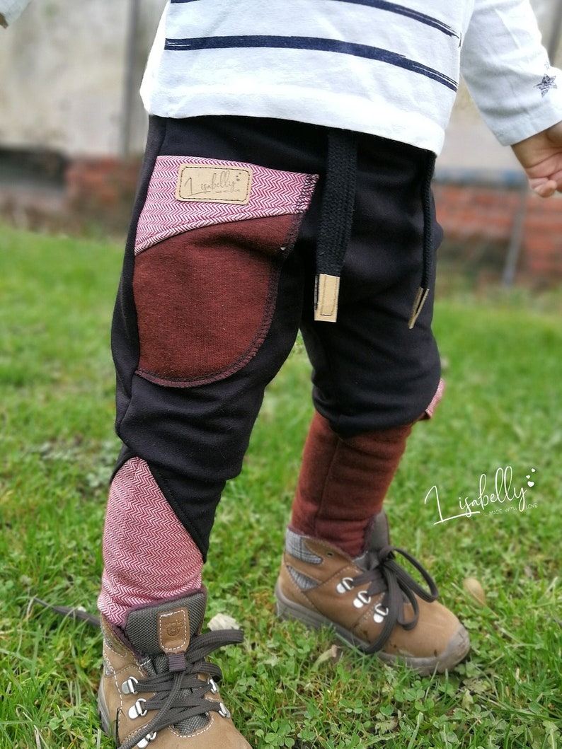Puede incluir: Pantalones de ch&aacute;ndal negros con detalles en tejido rojo y marr&oacute;n. Los pantalones tienen una cintura con cord&oacute;n y un peque&ntilde;o parche con el texto "lisabelly" en el bolsillo delantero izquierdo.