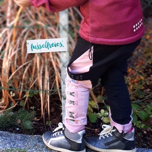 Puede incluir: Un ni&ntilde;o lleva una chaqueta y pantalones rosa y negro con la palabra "fusselfreies" en una etiqueta. Los pantalones tienen una raya rosa a un lado y el ni&ntilde;o lleva zapatillas negras y grises.