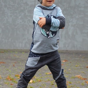 Puede incluir: Un ni&ntilde;o peque&ntilde;o con una sudadera con capucha azul y gris con un gr&aacute;fico de tem&aacute;tica espacial, gorro gris, jeans azul oscuro con un bolsillo de parche y zapatillas marrones.