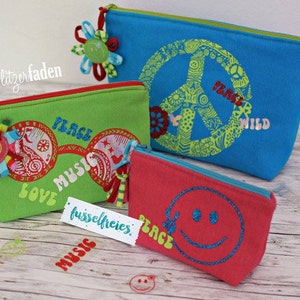 May include: Three colorful zippered pouches with peace signs, smiley faces, and the words "Peace Music Love" and "Peace Wild" printed on them. The pouches are made of fabric and have a zipper closure.