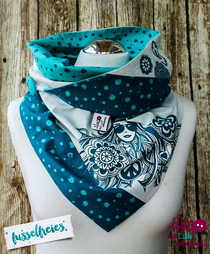 May include: A white, teal, and turquoise patterned scarf with a peace sign and a woman's face design. The scarf is folded and displayed on a white mannequin. The text "fussselfreies" is visible in the lower left corner of the image.