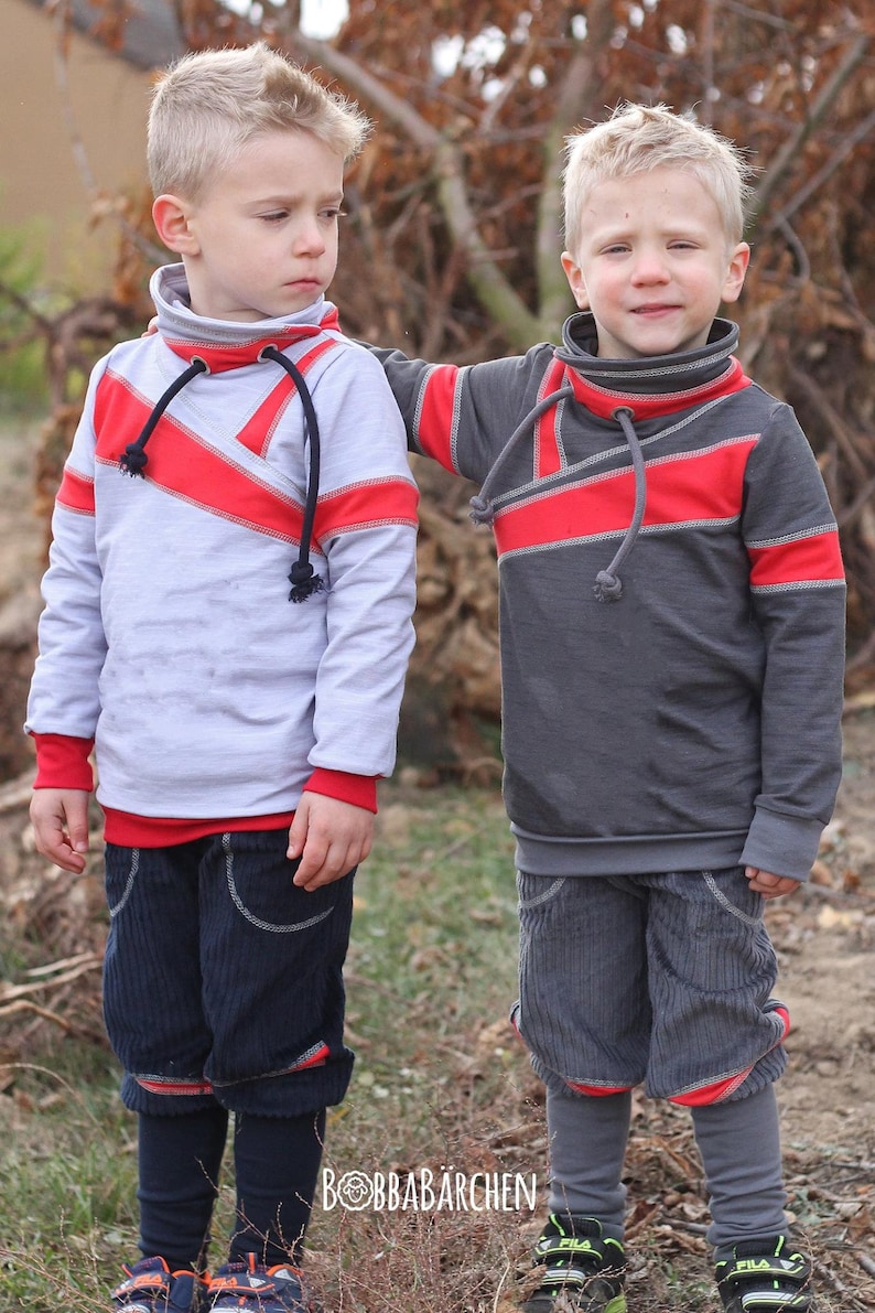 May include: Two young boys wearing gray and white long-sleeved shirts with red and gray trim. The shirts have a unique design with a diagonal red stripe across the front. The boys are wearing blue corduroy pants with red trim.
