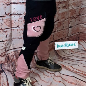 Puede incluir: Pantalones para ni&ntilde;os negros y rosas con un coraz&oacute;n y la palabra "LOVE" en el bolsillo. Los pantalones est&aacute;n hechos de una tela suave y c&oacute;moda, perfectos para el uso diario.