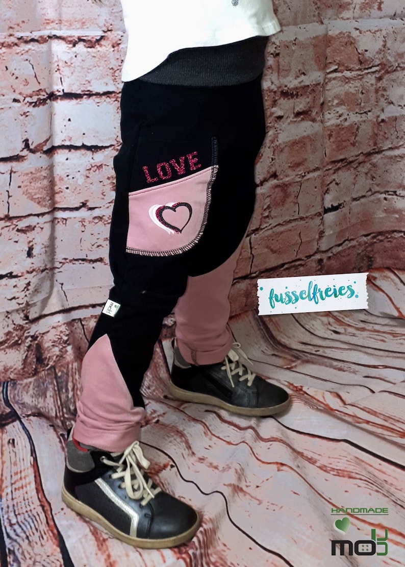 Puede incluir: Pantalones para ni&ntilde;os negros y rosas con un coraz&oacute;n y la palabra "LOVE" en el bolsillo. Los pantalones est&aacute;n hechos de una tela suave y c&oacute;moda, perfectos para el uso diario.