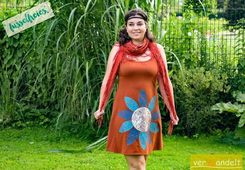 May include: A woman wearing a rust-colored dress with a blue and white floral design. She is wearing a red scarf and a headband. The text "fussselfreies" is visible in the background.