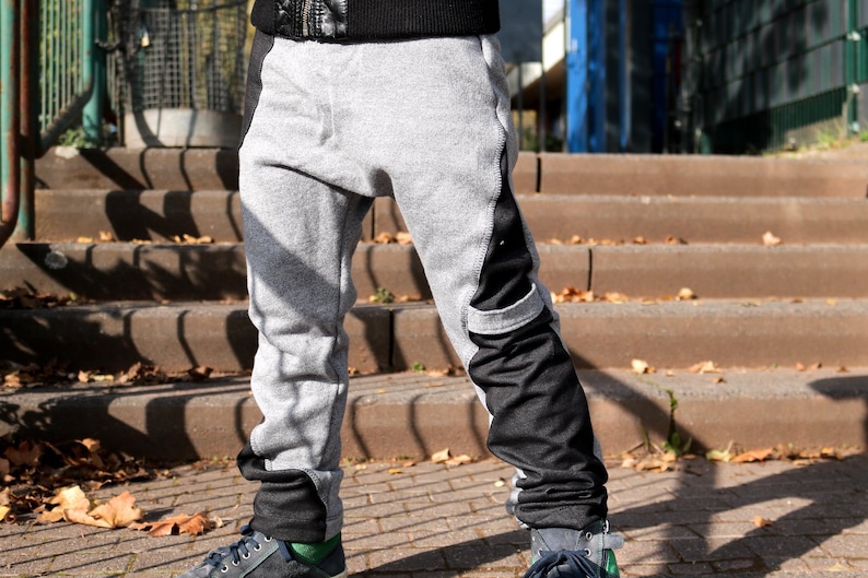 Puede incluir: Pantalones de ch&aacute;ndal grises con paneles de tela negra en los laterales y las piernas. Los pantalones tienen un corte holgado y est&aacute;n remangados en los tobillos.