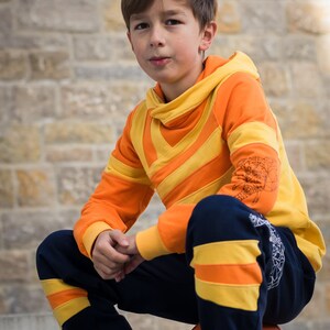 May include: A young person wearing a bright orange and yellow striped hoodie with a black and yellow striped waistband. The person is sitting on a basketball.