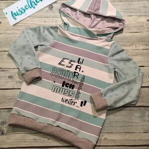 May include: A light blue and gray striped hooded sweatshirt with a star pattern on the sleeves. The sweatshirt has a text design that reads "Es war sch&ouml;n, aber ich muss weiter..."