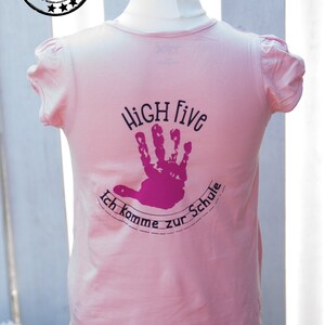 May include: Pink t-shirt with a black and pink design that says "HIGH Five Ich komme zur Schule".