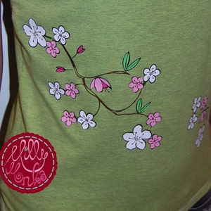Könnte beinhalten: Grünes Tanktop mit einem weißen und rosafarbenen Blumendesign. Das Design zeigt einen Zweig mit Blumen und Blättern. Das Tanktop hat ein rotes und weißes Etikett mit dem Text "Lilly Wonka" darauf.