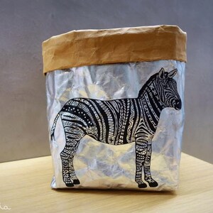 May include: A silver and brown paper bag with a black and white zebra design. The zebra is facing to the right and has a detailed pattern.