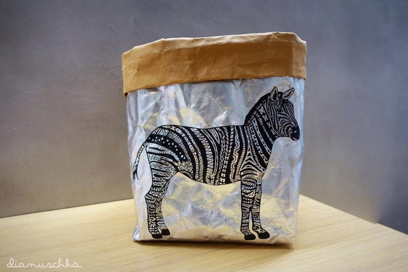 May include: A silver and brown paper bag with a black and white zebra design. The zebra is facing to the right and has a detailed pattern.