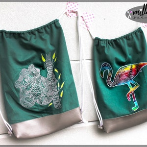 May include: Two green drawstring bags with white drawstrings. One bag features a white koala design and the other features a colourful flamingo design. Both bags have a silver bottom.